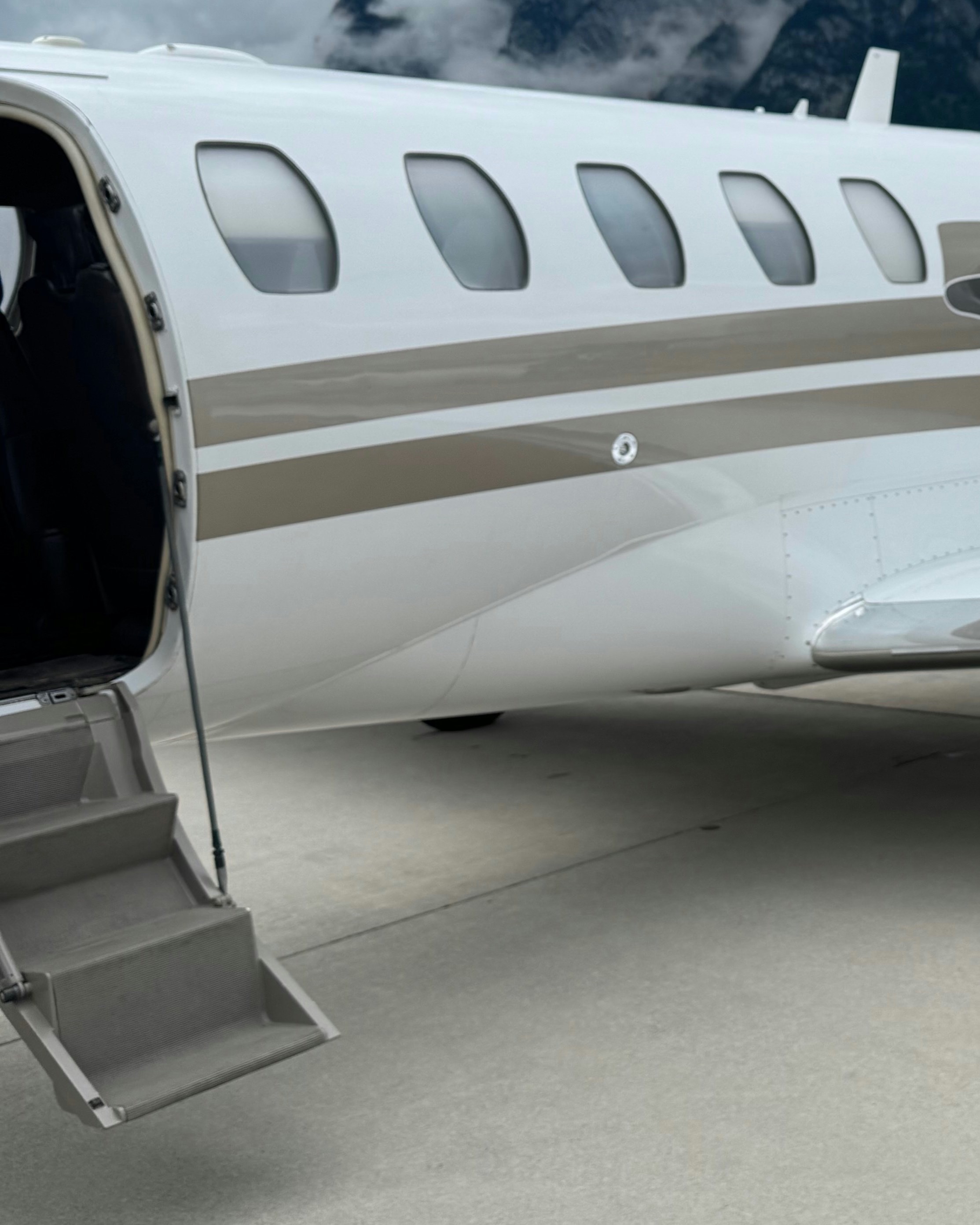 Open cabin door and airstairs of a private jet, mountains behind